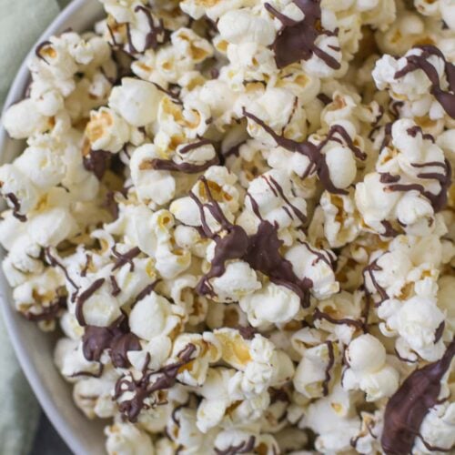 Chocolate Covered popcorn in a white bowl with a green linen off to the side.