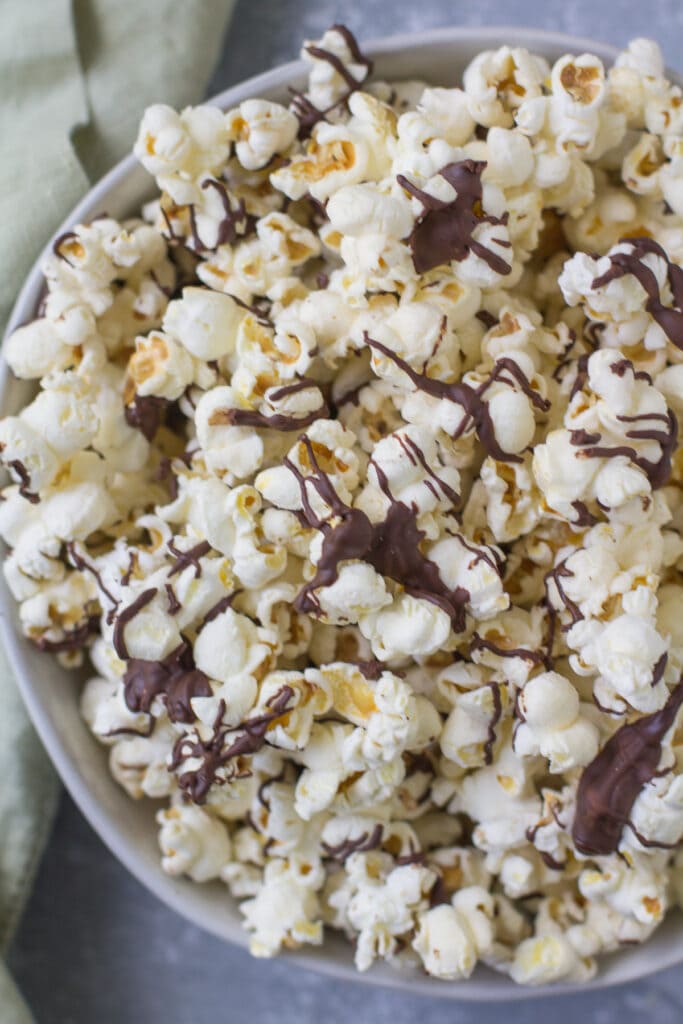 Chocolate Covered popcorn in a white bowl with a green linen off to the side.