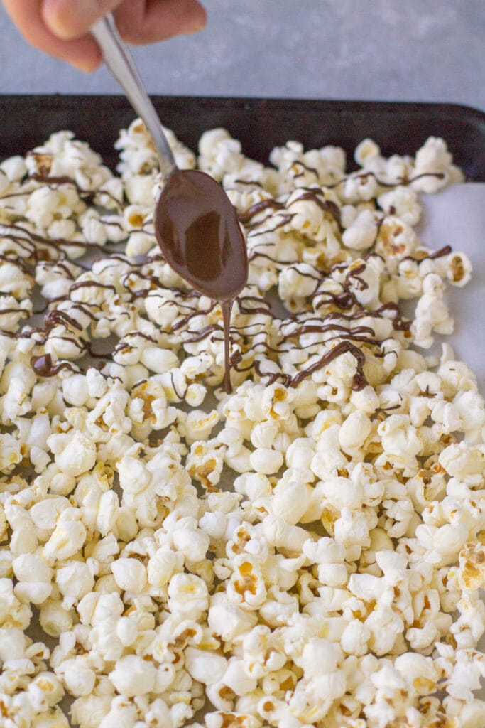 A spoon drizzling chocolate over chocolate covered popcorn