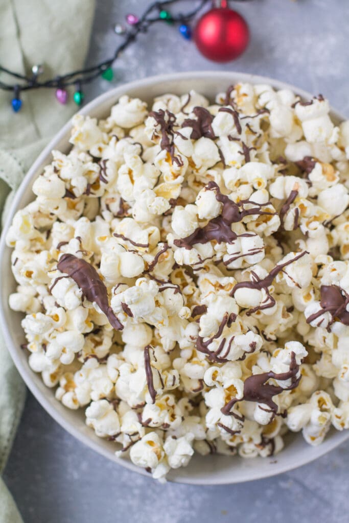 A bowl of popcorn with an ornament and christmas lights near it.