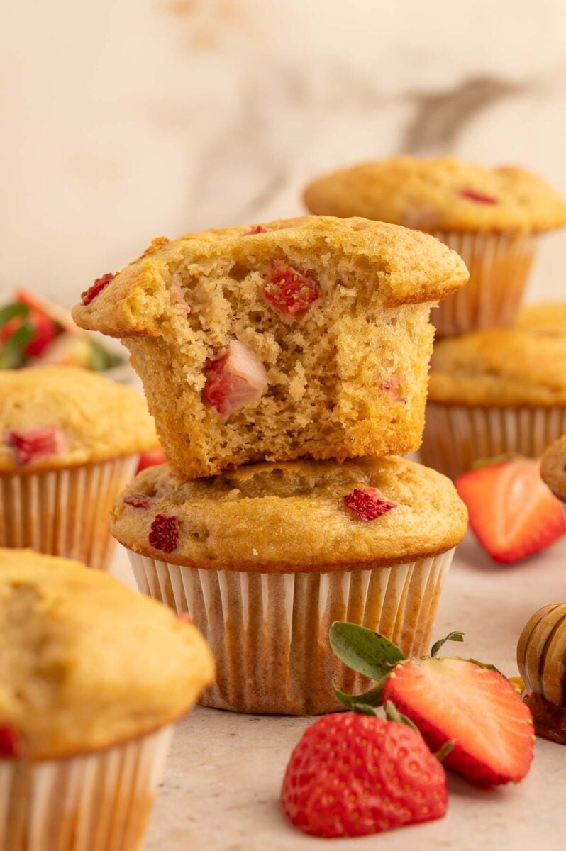 Two strawberry protein muffins stacked on each other with the top one having a bite taken out of it.