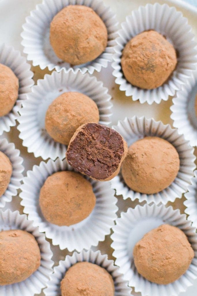 a healthy chocolate truffle with a bite of it taken out. plate of chocolate truffles in background