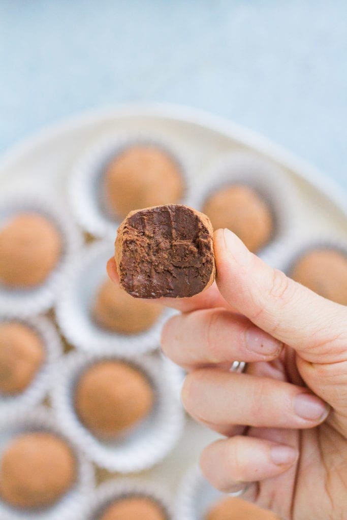 a hand holding up a healthy chocolate truffle with a bite of it taken out.