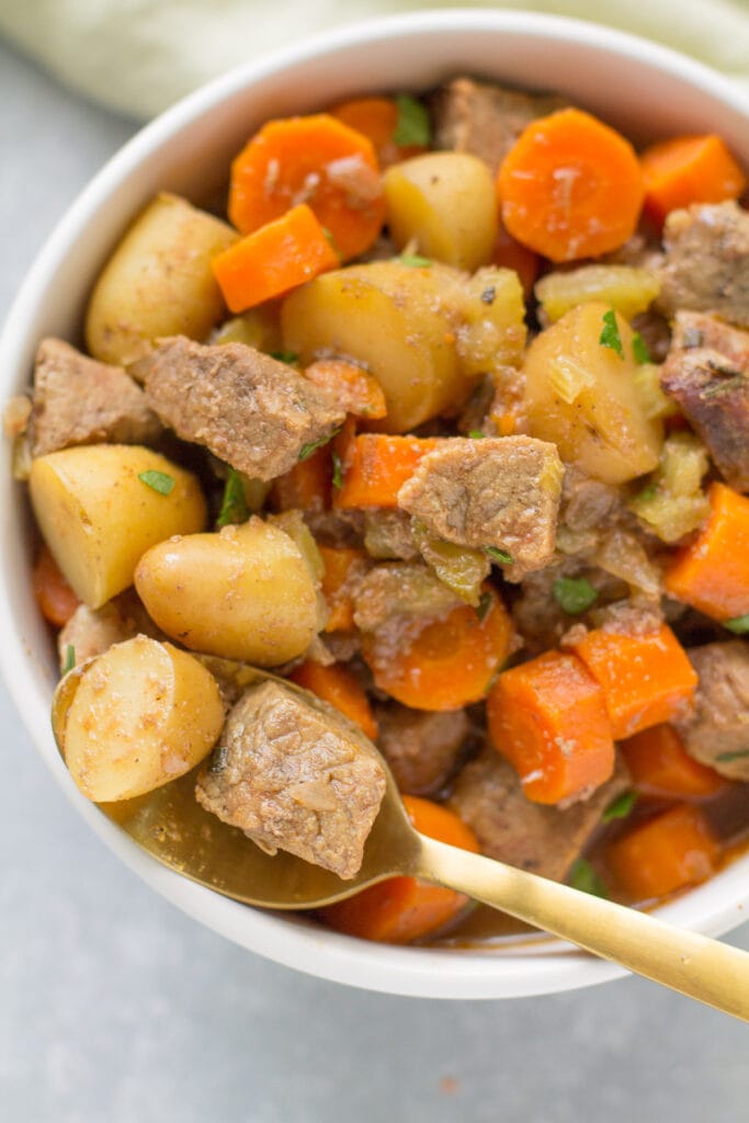A close up of a white bowl filled with paleo beef stew. A gold spoon off to the side taking a bite out of it.