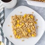 An overhead shot of mango pineapple oatmeal on a white plate with coffee and a baking dish off to the side.