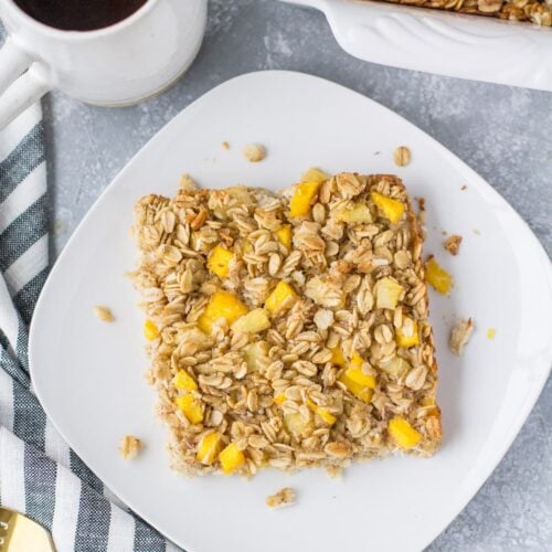 An overhead shot of mango pineapple oatmeal on a white plate with coffee and a baking dish off to the side.