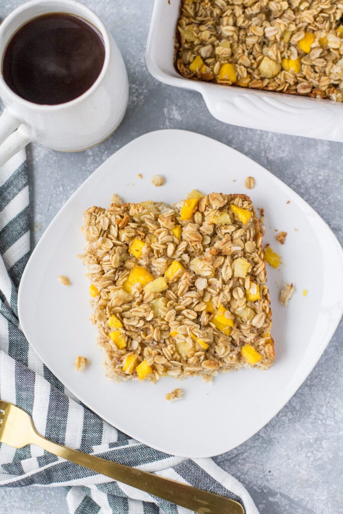 An overhead shot of mango pineapple oatmeal on a white plate with coffee and a baking dish off to the side.