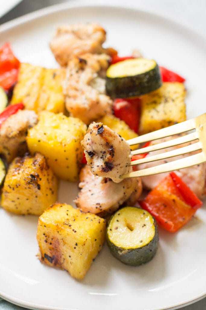 Chicken Pineapple Kebabs taken off the skewers on a white plate with a golden fork taking a bite out of them