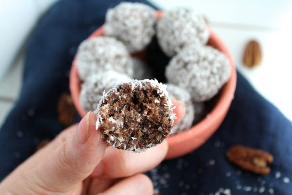 Whole 30 Chocolate Coconut Bites in a pink bowl with a hand holding up a bite that has been bitten into