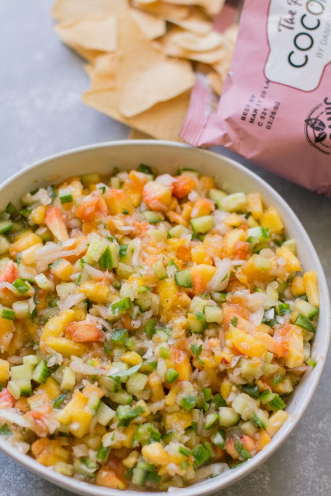 A big bowl of peach cucumber salsa with coconut chips off to the side