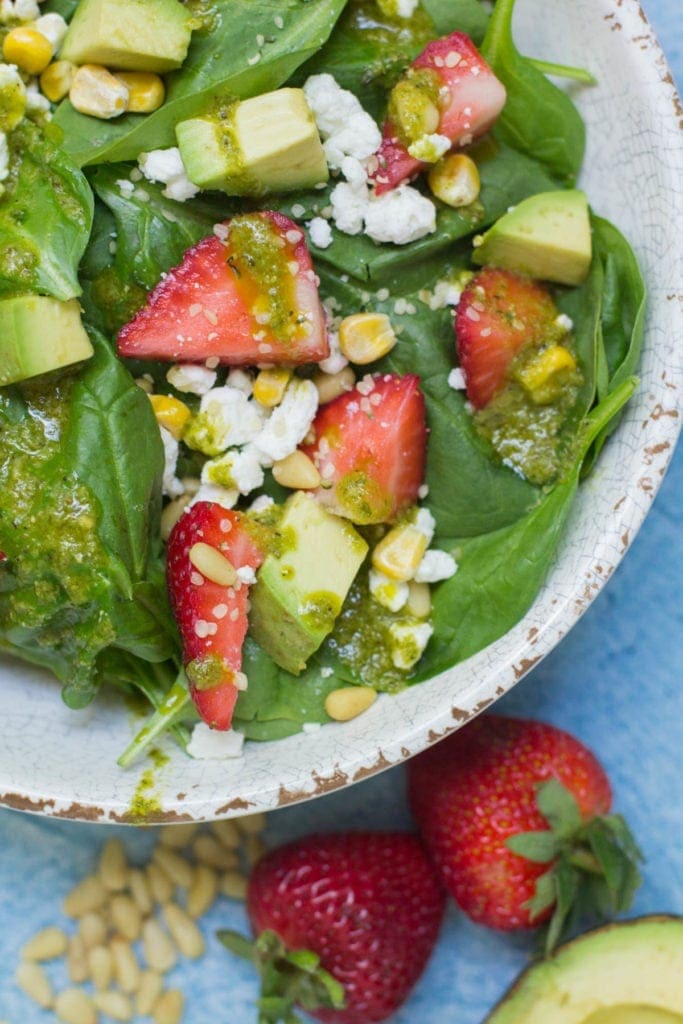 Overhead view of a bowl filled with strawberry, spinach, avocado, and goat cheese salad drizzled with lemon vinaigrette dressing.