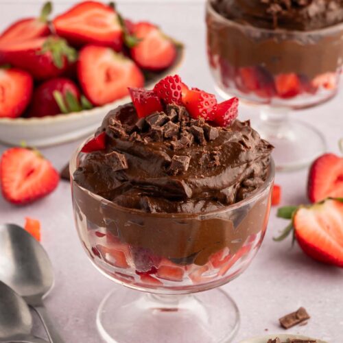 Chocolate Avocado Pudding in a clear serving dish topped with chopped strawberries and more berries in the background.