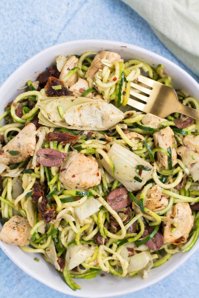 Whole30 Greek Chicken Zucchini Noodles in a white bowl with a fork taking a bite out of it.