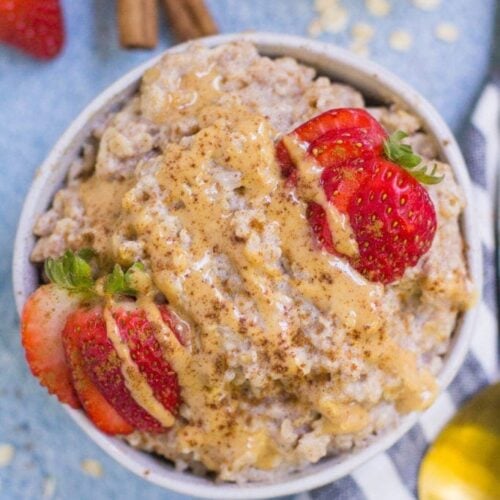 a white bowl filled with egg white oatmeal, topped with strawberries and nut butter