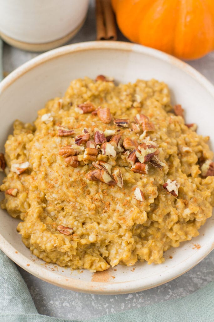 Crockpot steel cut oats in a white bowl on a blue background. A small pumpkin is in the background