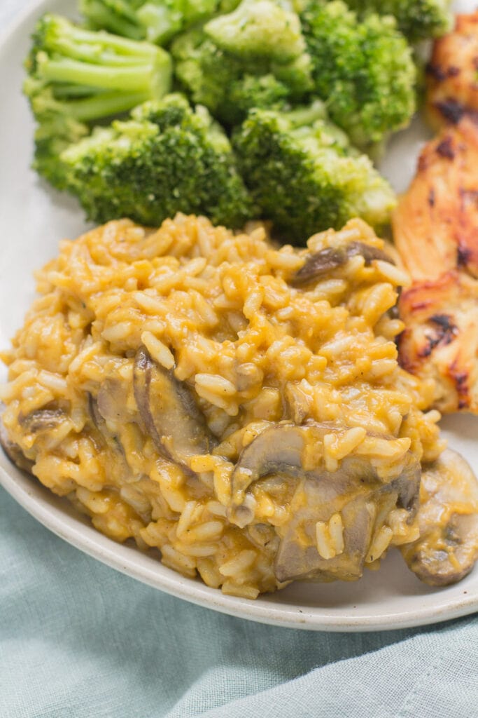 pumpkin risotto on a white plate with chicken and veggies in the background