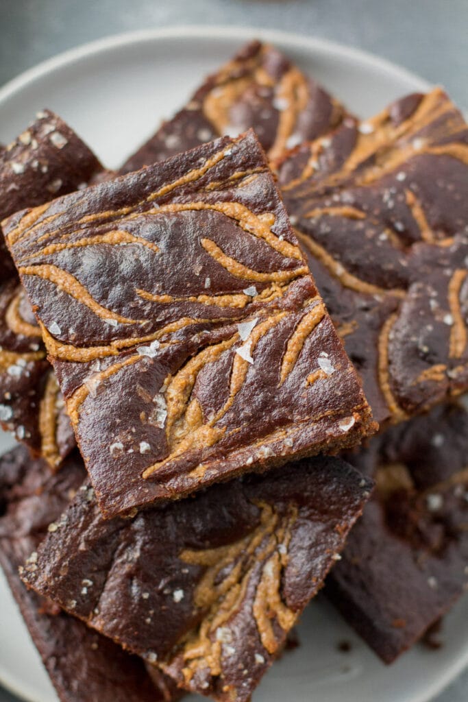 An overhead shot of almond butter brownies on a white plate on a grey background