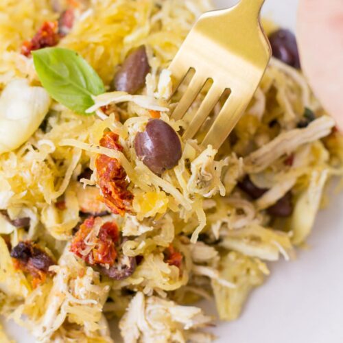 A fork taking a bite out of greek chicken spaghetti squash bake on a white plate.