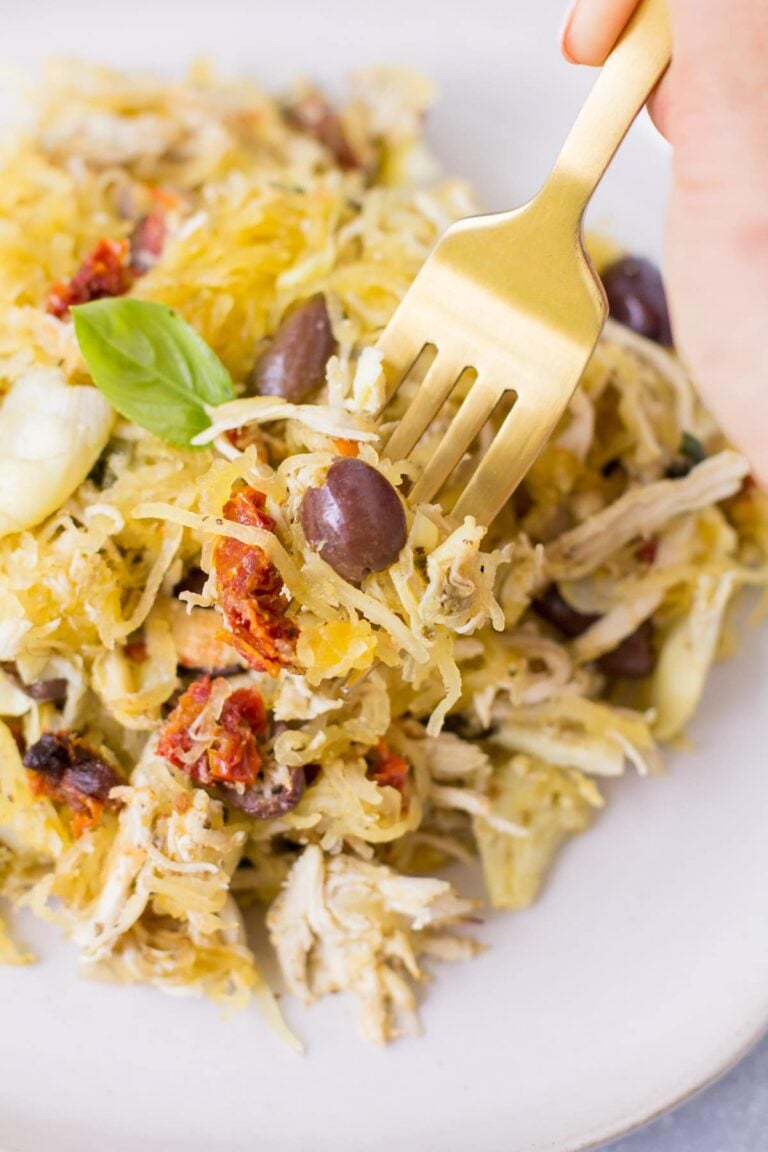 A fork taking a bite out of greek chicken spaghetti squash bake on a white plate.