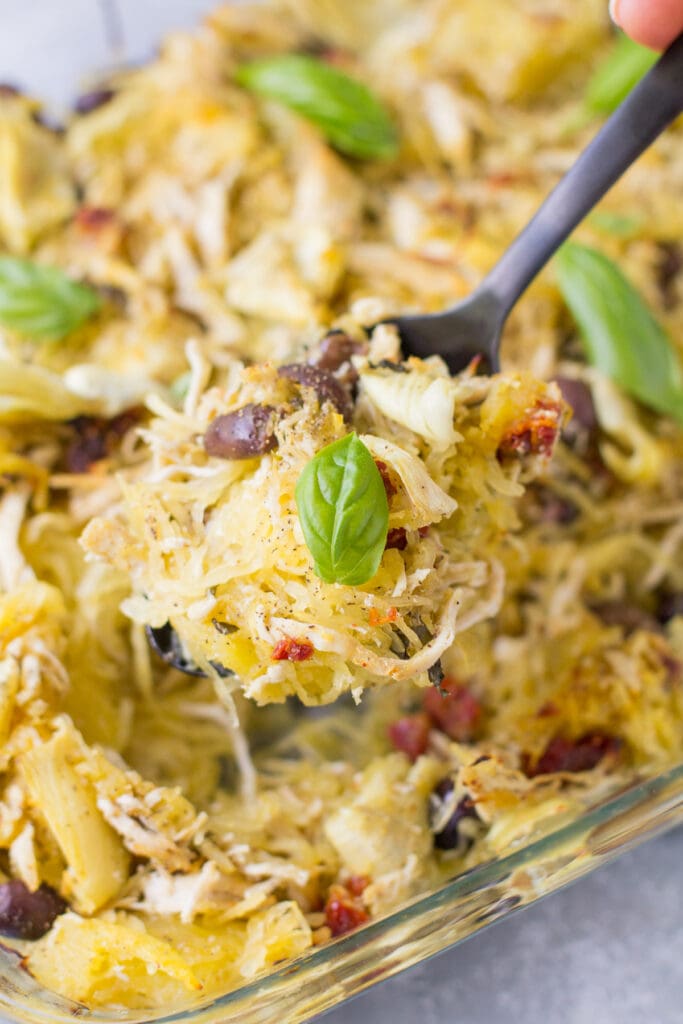 A black serving spoon taking a scoop out of greek chicken spaghetti squash bake