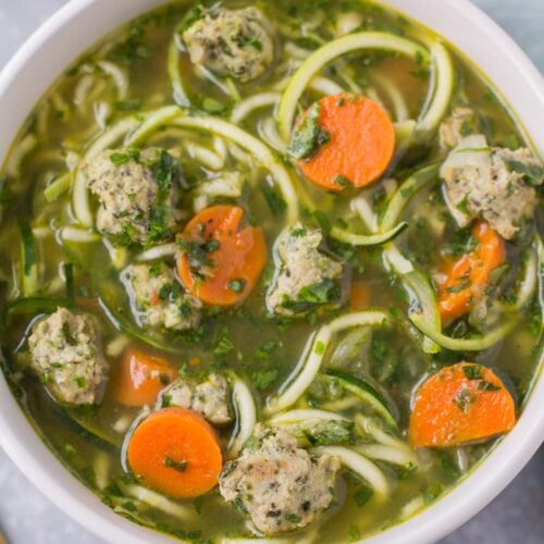 Healthy Italian Wedding Soup in a white bowl on a grey background with a linen off to the right side.