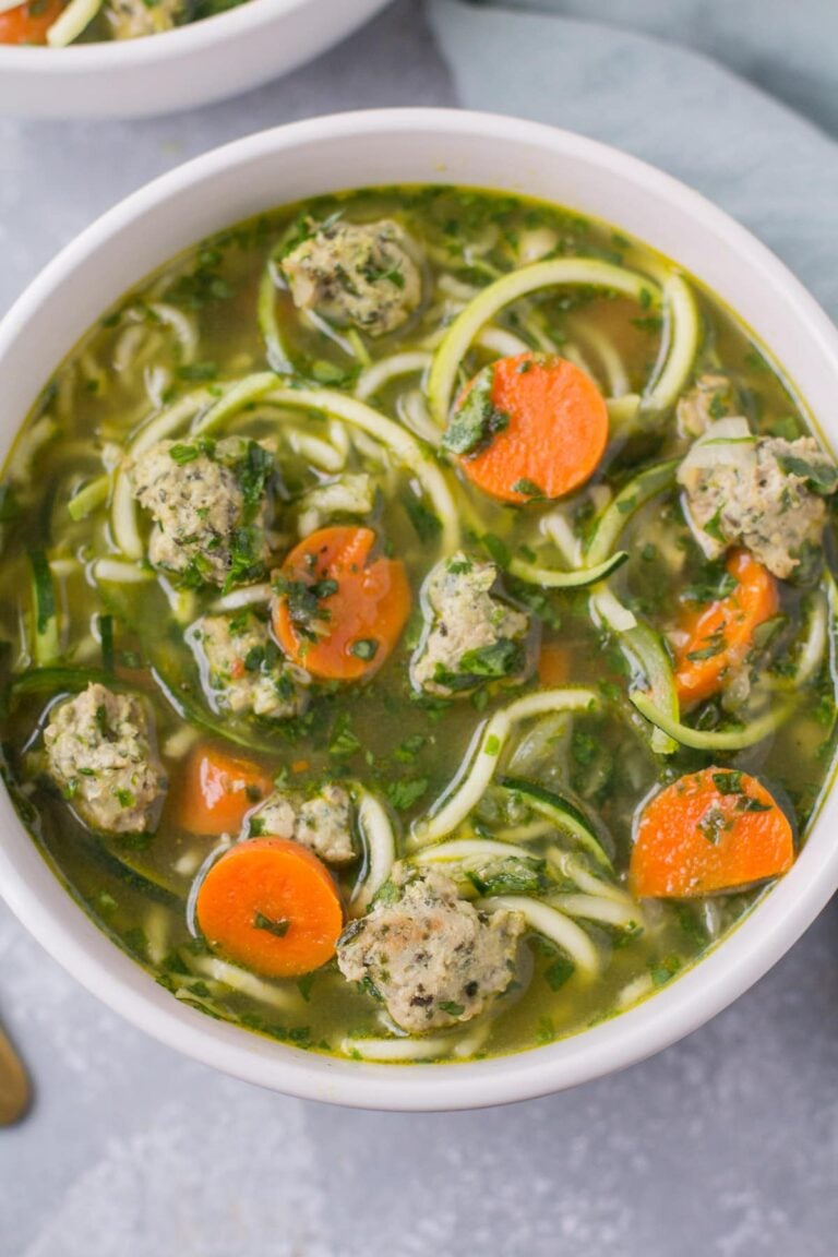 Healthy Italian Wedding Soup in a white bowl on a grey background with a linen off to the right side.