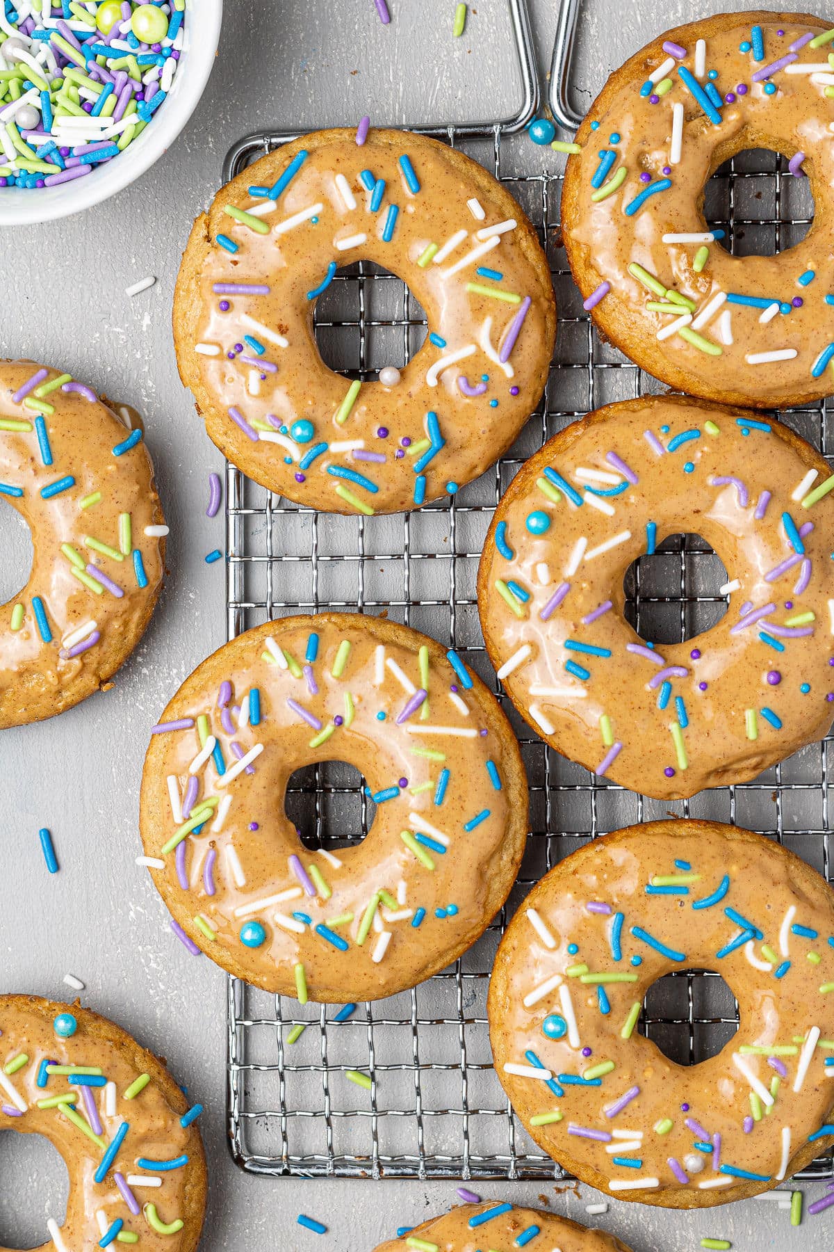 Homemade protein donuts, baked and topped with nut butter glaze and pastel colored sprinkles, viewed from overhead
