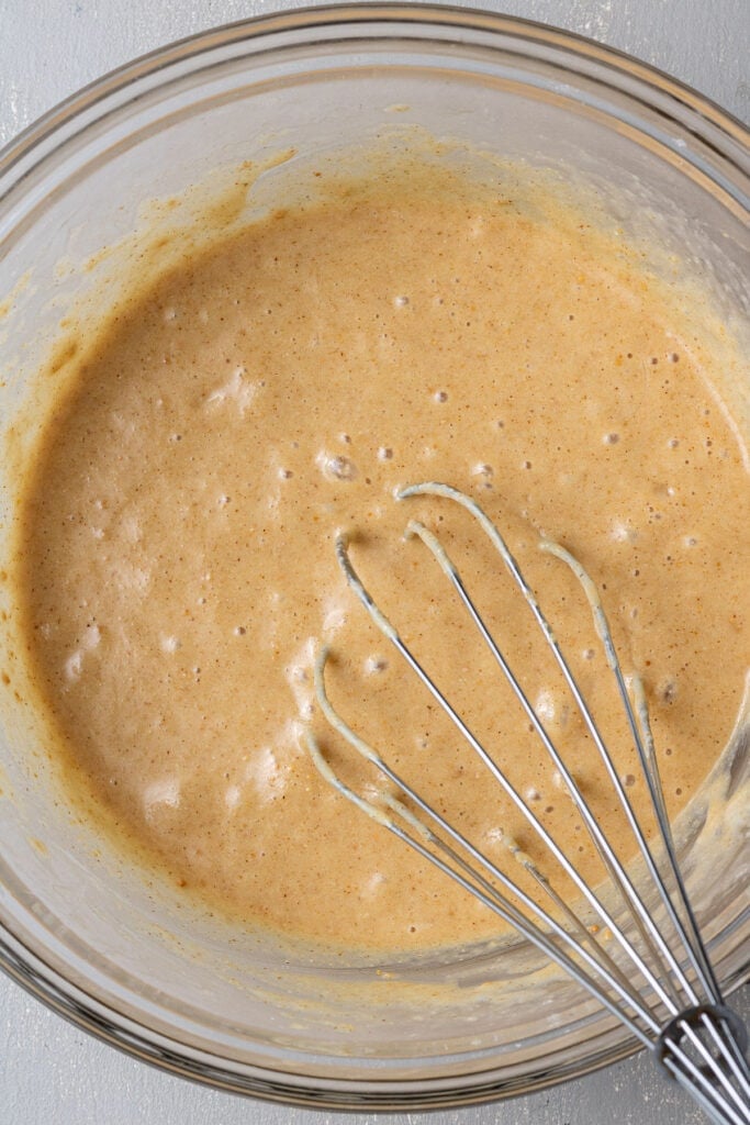 Overhead view of a wire whisk sitting in a glass mixing bowl filled with thick batter.