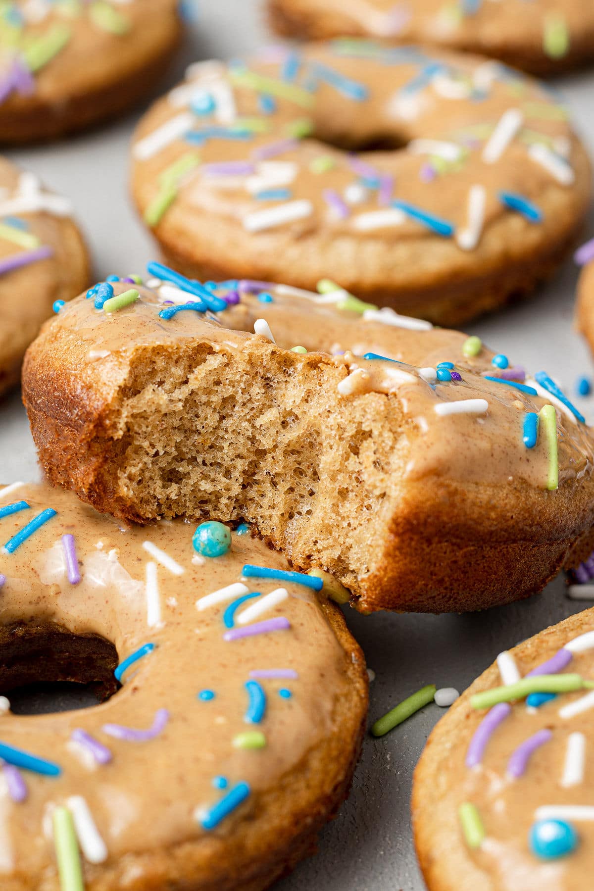 A homemade healthy donut topped with pastel colored sprinkles, with a bite taken out of it, shown close up.
