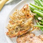Spiralized Potatoes on a white plate with green beans and chicken to the side.