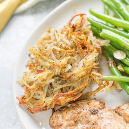 Spiralized Potatoes on a white plate with green beans and chicken to the side.