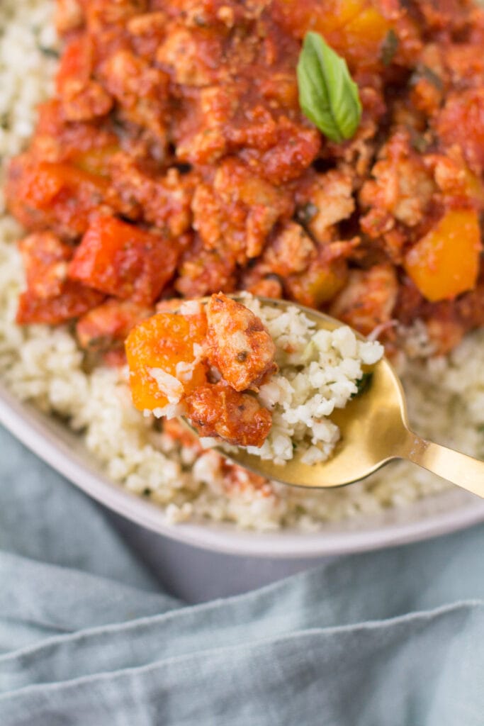 a gold spoon taking a bite out of unstuffed peppers with a blue linen off to the side.