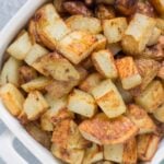 A white serving bowl filled with crispy roasted potatoes.
