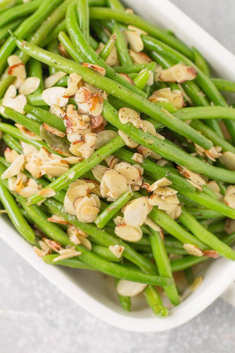 A white serving dish piled high with green beans almondine.