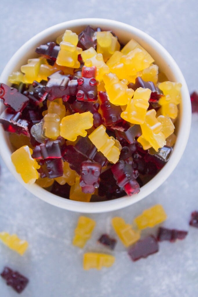 An overhead view of homemade gummy bears in a white bowl with gummy bears scattered around the bowl