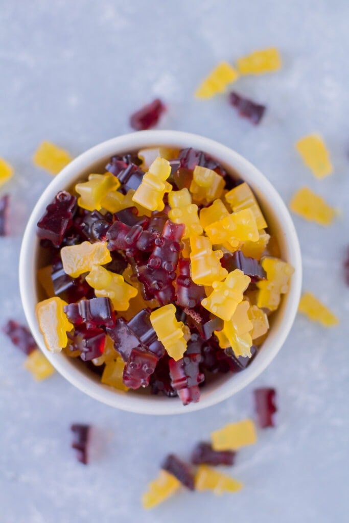 A top down shot of healthy gummy bears scattered around a small white bowl on a grey background