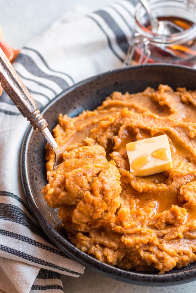 A spoon scooping up paleo sweet potatoes from a dark bowl