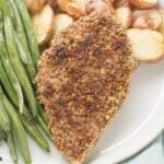 Pecan Crusted Chicken on a white plate with roasted potatoes and green beans.