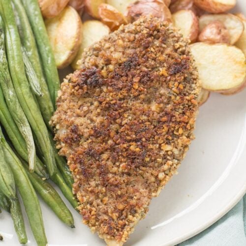Pecan Crusted Chicken on a white plate with roasted potatoes and green beans.