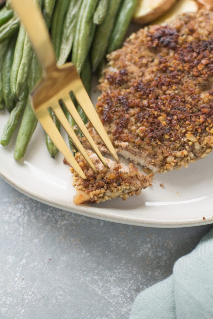 A gold fork taking a bite out of pecan crusted chicken cutlets.