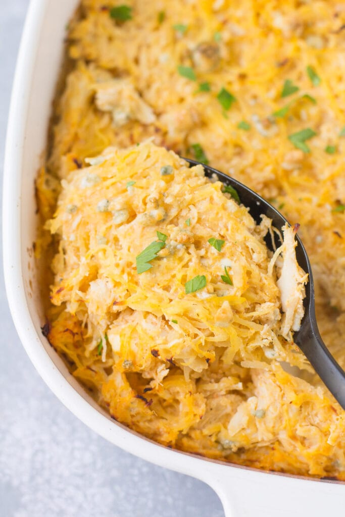 A black serving spoon taking a big scoop out of buffalo chicken spaghetti squash casserole.