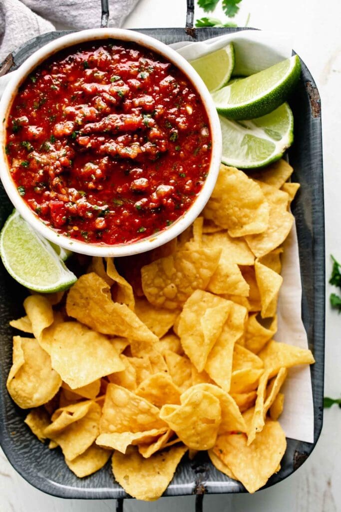 A close up of red chipotle salsa on a tray with chips and limes