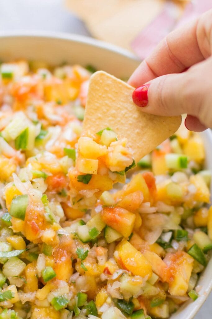 A chip scooping out a bite of healthy peach cucumber salsa