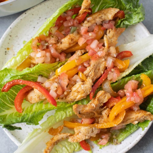 Whole30 Chicken Fajitas on a white plate with a grey background and a pan of fajitas in the background