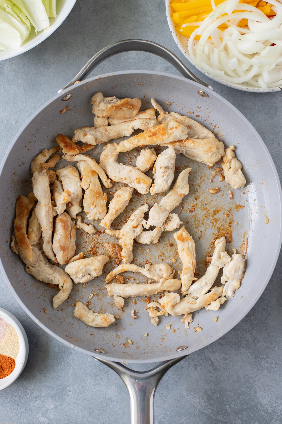A pan of cut chicken breast in a pan with other ingredients for healthy chicken fajitas on the side