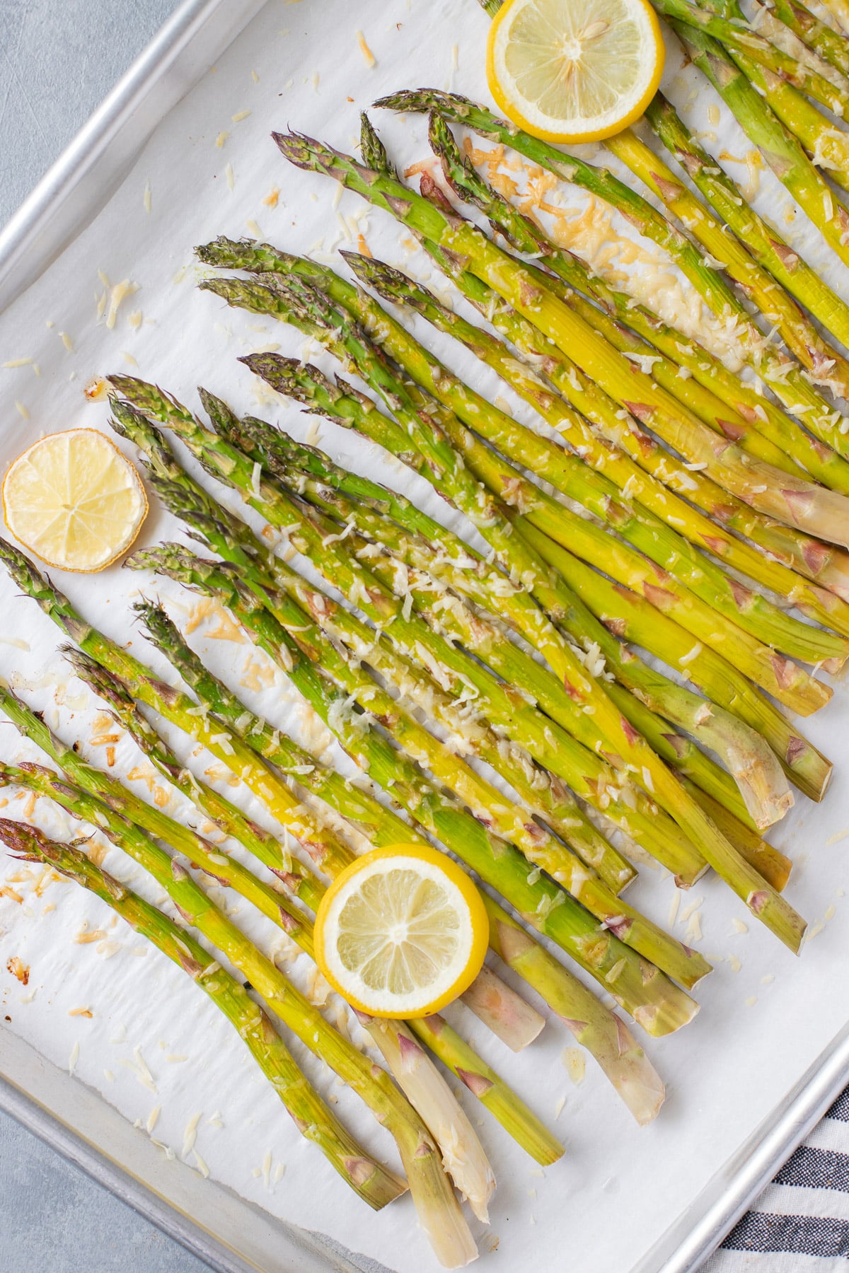 Fully cooked lemon asparagus with sliced lemons on a parchment lined baking sheet after being cooked