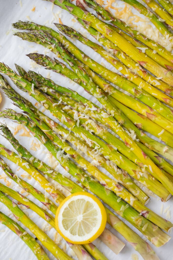 Healthy Lemon Parmesan Roasted Asparagus on a parchment lined baking sheet with a sliced lemon on top