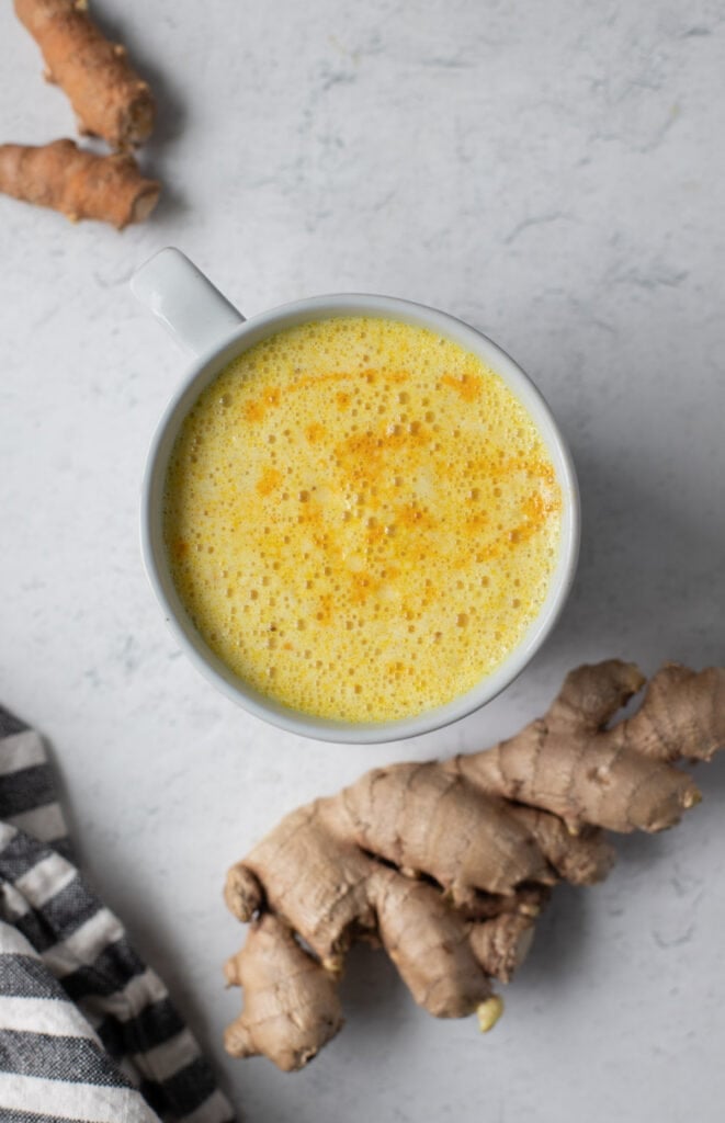 An overhead image of an easy turmeric latte on a white background with ginger and turmeric off to the side