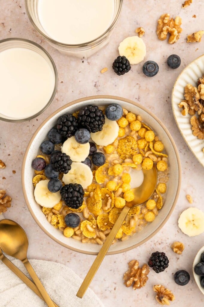 A bowl of cereal, blueberries, and sliced bananas in walnut milk with two glasses of homemade walnut milk on the side.