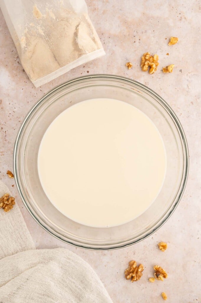 A clear bowl of homemade walnut milk with a used nut milk bag on the side.